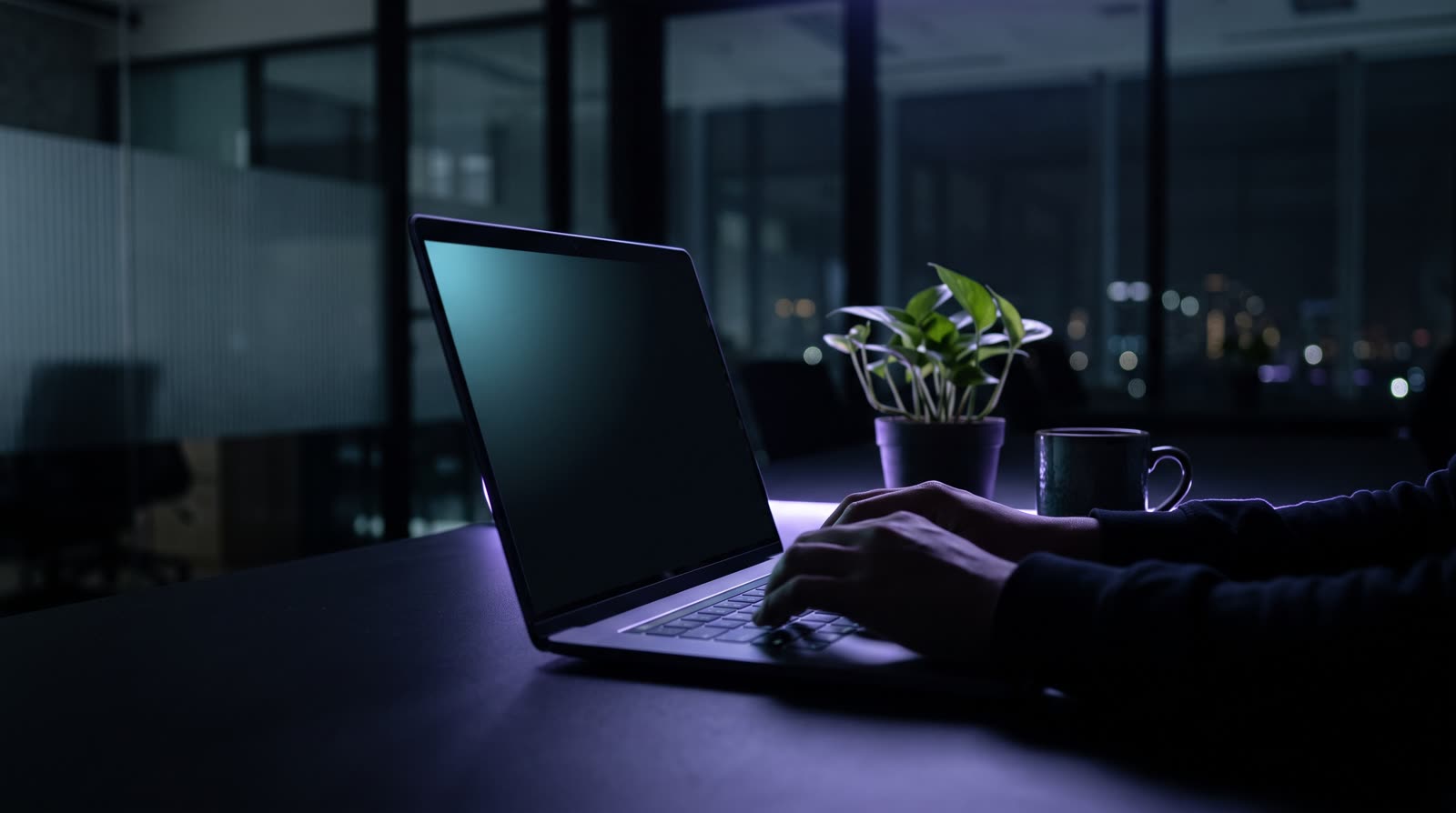 Laptop modern tunggal di meja gelap di ruang kerja Indonesia malam hari, layar menyala sian lembut, cahaya rim ungu dari belakang.